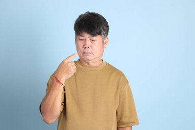 Mavi arka planda sıradan giyinmiş kıdemli Asyalı adam..