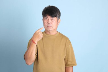 Mavi arka planda sıradan giyinmiş kıdemli Asyalı adam..