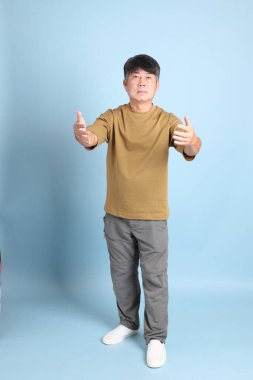 Mavi arka planda sıradan giyinmiş kıdemli Asyalı adam..