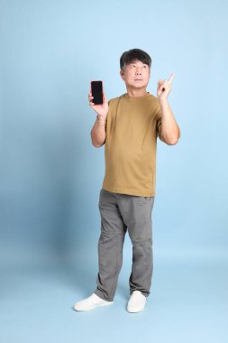 Mavi arka planda sıradan giyinmiş kıdemli Asyalı adam..