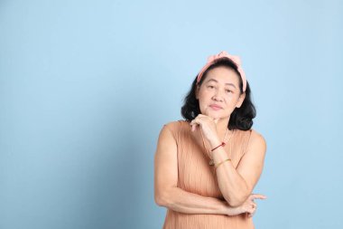 Kahverengi giyinmiş, mavi arka planda duran kıdemli Asyalı kadın..