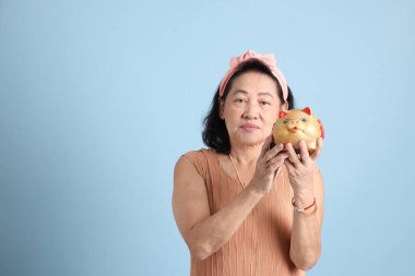 Kahverengi giyinmiş, mavi arka planda duran kıdemli Asyalı kadın..