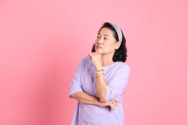 Pembe arka planda kahverengi giyinmiş yaşlı Asyalı kadın..