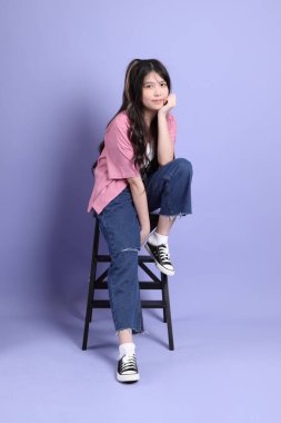 Mor arka planda oturan sıradan giysili tatlı Asyalı kız..