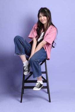 Mor arka planda oturan sıradan giysili tatlı Asyalı kız..