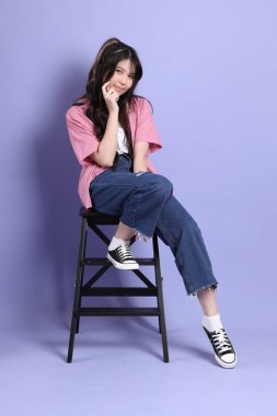 Mor arka planda oturan sıradan giysili tatlı Asyalı kız..