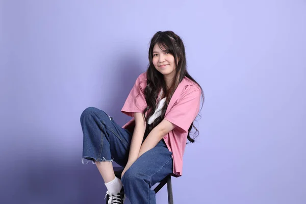 那个穿着休闲装坐在紫色背景上的可爱的年轻亚洲女孩 — 图库照片