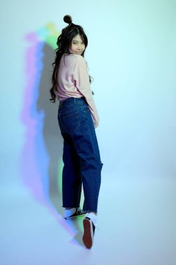 Stüdyoda jel rengi yıldırımın altında poz veren sıradan giyinmiş genç Asyalı kız..