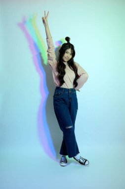 Stüdyoda jel rengi yıldırımın altında poz veren sıradan giyinmiş genç Asyalı kız..