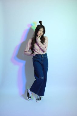 Stüdyoda jel rengi yıldırımın altında poz veren sıradan giyinmiş genç Asyalı kız..