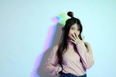 Stüdyoda jel rengi yıldırımın altında poz veren sıradan giyinmiş genç Asyalı kız..