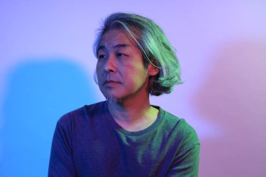 Beyaz arka planda, renk jöleli ışıklandırmanın altında havalı kıdemli Asyalı adam..