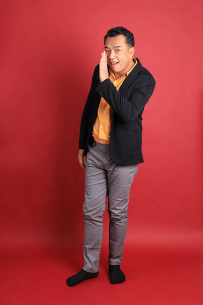 The Asian middle aged man standing on the red background.