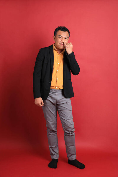 The Asian middle aged man standing on the red background.