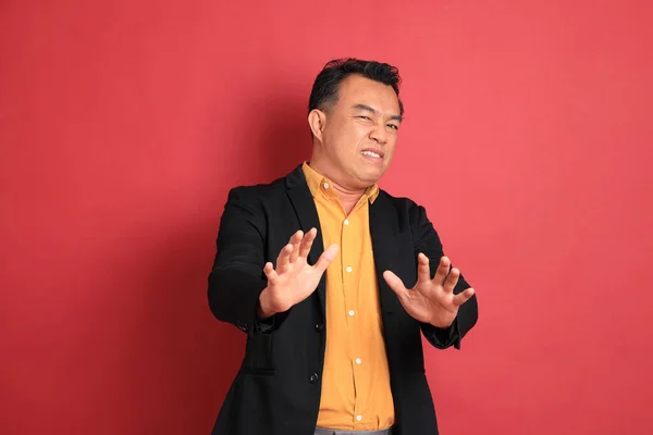 The Asian middle aged man standing on the red background.