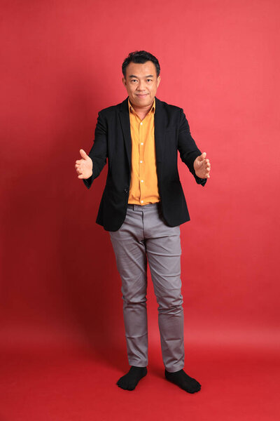 The Asian middle aged man standing on the red background.