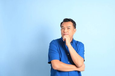 Mavi arka planda duran Asyalı orta yaşlı adam..