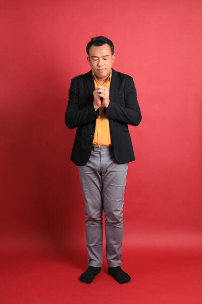 The Asian middle aged man standing on the red background.