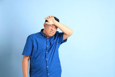 Mavi arka planda duran Asyalı orta yaşlı adam..