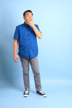 Mavi arka planda duran Asyalı orta yaşlı adam..