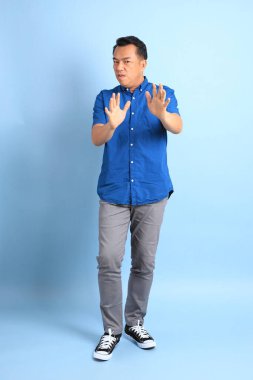 Mavi arka planda duran Asyalı orta yaşlı adam..