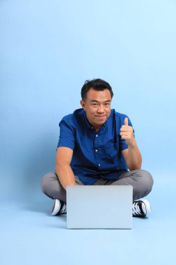 Yerde oturan mavi gömlekli Asyalı orta yaşlı adam..