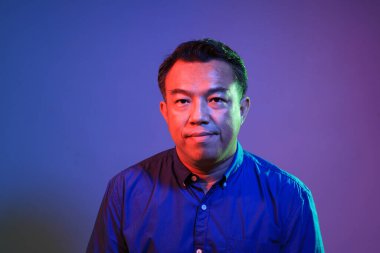 Renkli jel ışıklandırmasının altında mavi arka plandaki havalı kıdemli Asyalı adam.. 