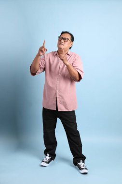The adult Asian man with pink shirt standing on the blue background.