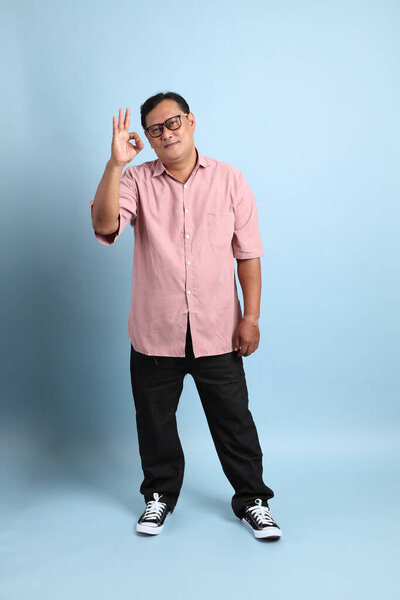 The adult Asian man with pink shirt standing on the blue background.