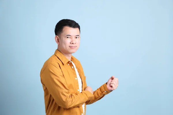 The Asian LGBTQ man with yellow shirt standing on the blue background.