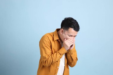The Asian LGBTQ man with yellow shirt standing on the blue background.