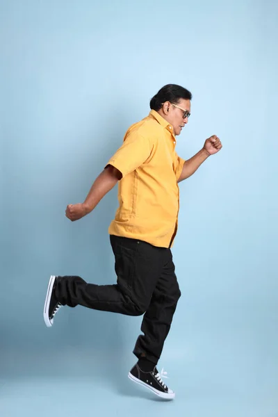 The adult Asian man with yellow shirt jumping on the blue background.