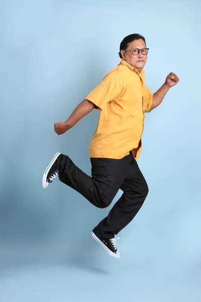 Adult Asian Man Yellow Shirt Jumping Blue Background — Stockfoto