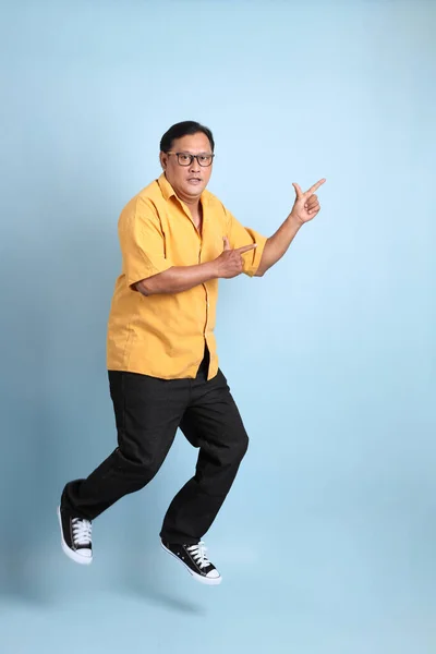 The adult Asian man with yellow shirt jumping on the blue background.