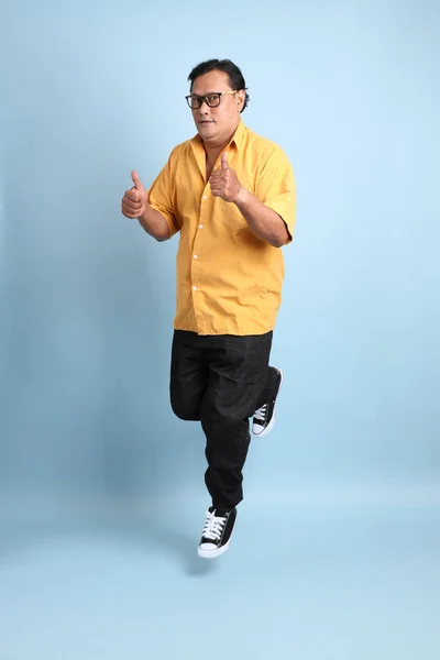 The adult Asian man with yellow shirt jumping on the blue background.