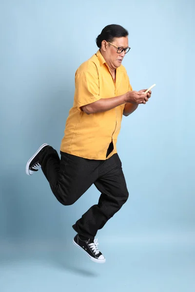 Adult Asian Man Yellow Shirt Jumping Blue Background — Stockfoto