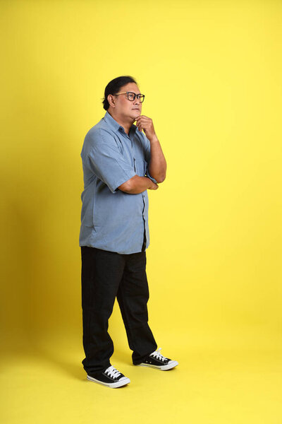The adult Asian man with blue shirt standing on the yellow background.