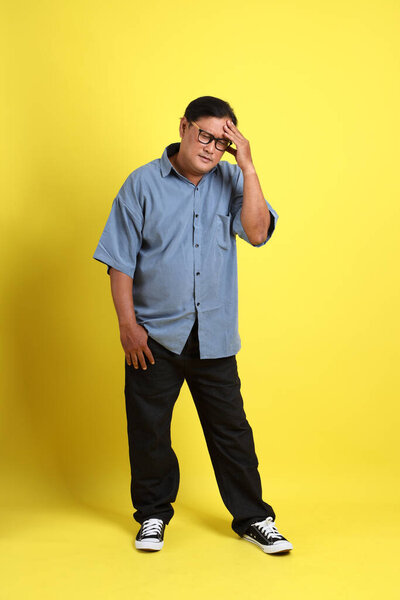 The adult Asian man with blue shirt standing on the yellow background.