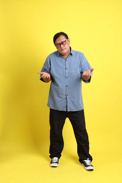 The adult Asian man with blue shirt standing on the yellow background.