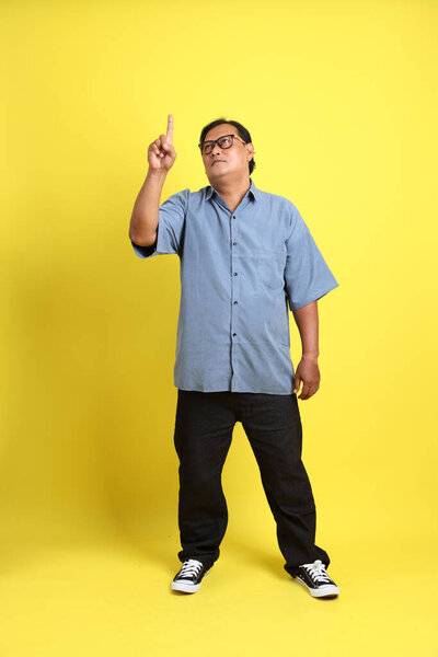 The adult Asian man with blue shirt standing on the yellow background.