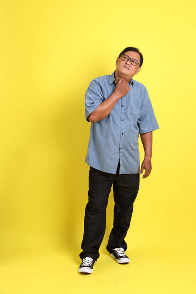 The adult Asian man with blue shirt standing on the yellow background.