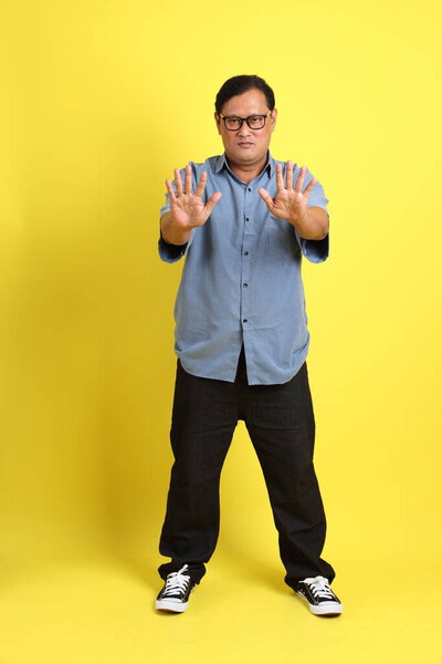 The adult Asian man with blue shirt standing on the yellow background.