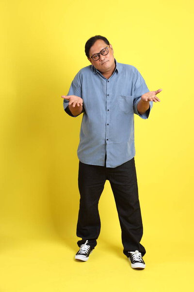 The adult Asian man with blue shirt standing on the yellow background.