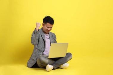Sarı arka planda oturan gri ceketli Asyalı LGBTQ adamı..