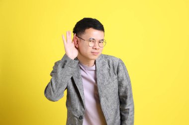 The Asian LGBTQ man with grey blazer standing on the yellow background.