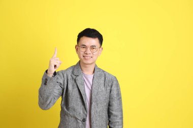 Sarı arka planda gri ceketli Asyalı LGBTQ adamı..