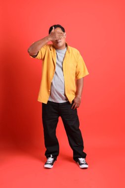 The adult Asian man with yellow shirt standing on the orange background.