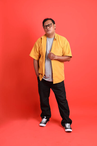 The adult Asian man with yellow shirt standing on the orange background.