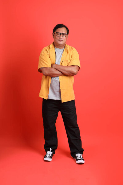 The adult Asian man with yellow shirt standing on the orange background.