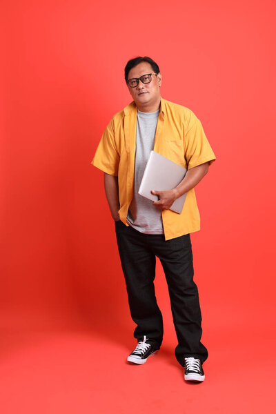 The adult Asian man with yellow shirt standing on the orange background.
